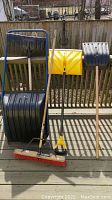 Full lot showing five items: three snow shovels and two brooms against wooden railing outdoors