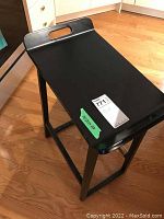 Black wooden stool angled from side showing carry handle cutout on seat and leg support bars.
