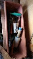 Bin with assorted garden tools including cultivator, pruning shears, dibber, tape roll