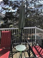 Photo of green patio umbrella with black metal stand on a balcony with outdoor chairs around.