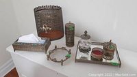 Photo showing metal waste basket, rectangular mirrored tray, decorative cylindrical container, tissue box holder, candle holder, and small metal ring accessory.