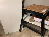 View showing black coated steel frame work table with plywood top and extra white composite table top leaning against the wall
