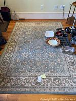 Full view of the Karastan area rug placed on a wooden floor with some household items on it, showing overall design and scale.