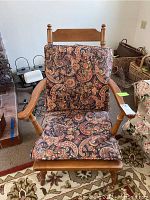 Front view of the wooden chair with patterned cushions. Shows the paisley upholstery and armrests.