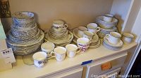 Wide view of grouped china sets on shelf including stacks of plates, cups, saucers in two Haviland china patterns and one Royal Doulton Ting pattern