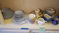 Full lot of assorted plates, bowls, cups, saucers, and serving pieces arranged on shelf.