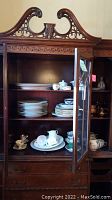Wardrobe with glass doors containing stacked plates, teacups, teapot and trinket boxes on shelves