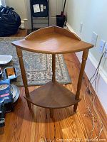 Full view of the two-tier wooden corner table showing triangular shape and top tier with back panel.