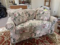 Front angle view of floral patterned Crate & Barrel loveseat with cushions on a red patterned rug.
