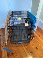 Metal dog crate with plastic bottom, adjustable wooden dog doorway gate leaning beside it