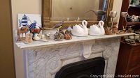 Wide shot of mantelpiece showing all figurines including swan planters, birds, donkeys, elephant, and horse.