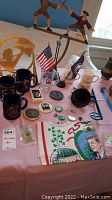 Photo showing the overall assortment of colonial soldier figurines, mugs, flags, buttons, pins, and other souvenirs arranged on a pink cloth surface.