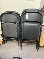 Seven black metal folding chairs, showing the folded seats and backrests. Four chairs have smooth vinyl seats, three chairs have patterned upholstered seats.