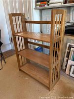 Side angled view of the wooden folding shelf showing three wide shelves and slatted side panels.