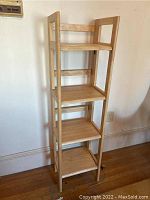 Front view of the four tier wooden folding shelf against a wall