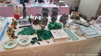 Wide view of multiple items on a display table including brown pottery, green shamrock-themed decor, glass sun catchers, and leprechaun figurines