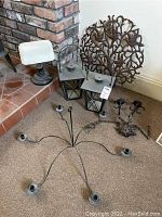 Shows two metal lanterns with glass and metal frames, small metal lamp with white shade, decorative metal wall hanging, and multiple candle holders including chandelier frame and candelabra.