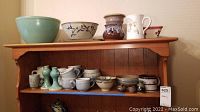 Wide shot of shelf with various pottery including bowls, mugs, pitchers, and candle holders