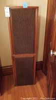 Pair of vintage wooden speakers with brown cloth grilles, standing on hardwood floors beside a wooden door.
