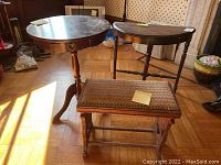 Full view showing two wooden tables and one upholstered footstool arranged on wood floor with light from window.