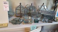 Multiple metal and glass miniature terrariums of various geometric shapes and trinket boxes displayed on a shelf.