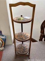 Full view of the three-tiered wooden collapsible shelf showing the top two tiers and part of the base tier with decorative painted round trays.