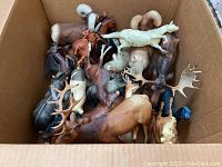 Top view of a cardboard box filled with assorted plastic animal figurines including horses, deer, and moose.