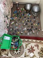 Die-cast toy soldiers and knights arranged on carpet with two silver plastic knights helmets and a cylindrical container with figures inside.