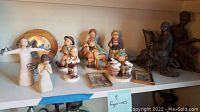 Overview of all figurines and framed prints on shelf including Willow Tree and Hummel figurines plus musician sculptures
