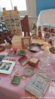 Various decorative and collectible items spread on a pink tablecloth including wood figurines, snow globes, small boxes, and glassware