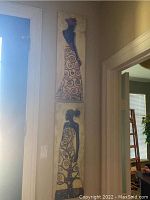 Photo of two vertical canvas prints showing stylized female figures with patterned dresses, colors purple and earth tones