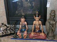 Wide view showing a metal abstract sculpture of two cyclists on a bike, two seated painted wood figurines, and a carved bust sculpture on a mantle.