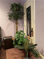 Photo showing three faux plants: tall palm tree near corner, potted faux plants around base, and corner view of hanging basket.