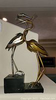 Full view of metallic bird sculpture with gold and silver tones, mounted on a black rectangular base