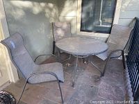 View of entire outdoor furniture set including round glass top table and three sling back chairs arranged on patio.