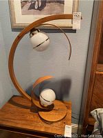 Front view of one lamp showing bentwood frame, upper and lower white globe light fixtures, and natural wood base