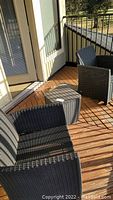 Two dark rattan armchairs and matching side table on wooden deck with shadows.