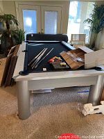 Three-quarter front view of silver-framed pool table with accessories on top