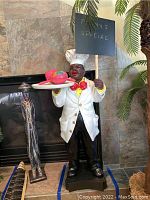 Full view of the chef sculpture standing in front of a fireplace, holding a menu sign and tray with maracas
