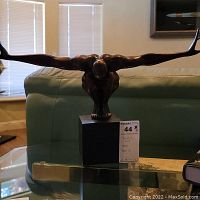 Bronze-tone painted winged figure sculpture atop rectangular base on glass table