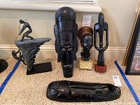 Five sculptures grouped on carpet, frontal view showing all items including mask, bust, wood figures, and reclining carving