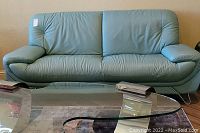 Front view of light blue leather sofa with padded armrests and metal legs.
