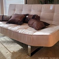 Front angle of contemporary light beige ultra suede sofa with brown cushions on it, highlighting upholstery texture and style.