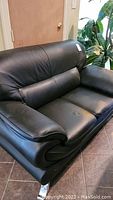 Front angled view of black leather sofa showing padded arms, backrest, and cushions, placed on tiled floor.