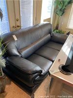 Front angle view of black bonded leather-like sofa showing seating cushions, rolled arms, and part of the room surroundings.