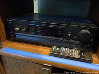 Sony audio video control center front view with remote control on wooden shelf.