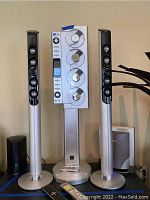 Front view of Sharper Image Quattro 4 CD player with iPod dock and paired tall tower speakers with silver base and black speaker fronts.