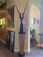 Full view of antelope sculpture atop pedestal showing placement and scale next to wall and framed artwork.