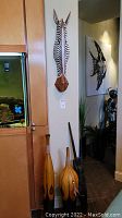 Room corner showing two tall wooden vases and a mounted wooden zebra head plaque.