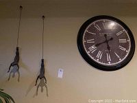 Photo showing two suspended diver wall art figures hanging next to a large round wall clock on a beige wall.